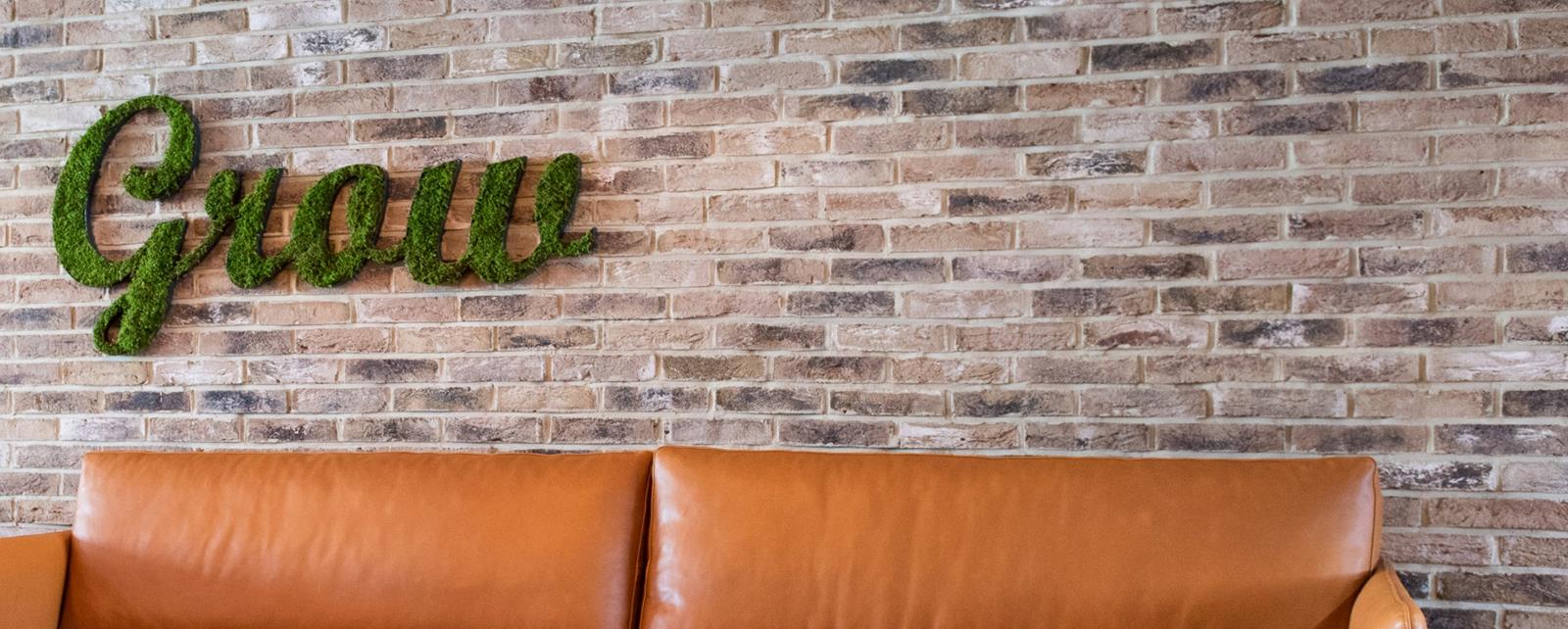 Leather Couch Against Brick Wall With Sign Made Of Plants On Wall
